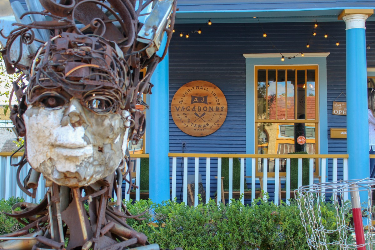 There's an abstract structure that resembles a man made of wires in front of a blue store called Vagabonds in Bishop Arts District.