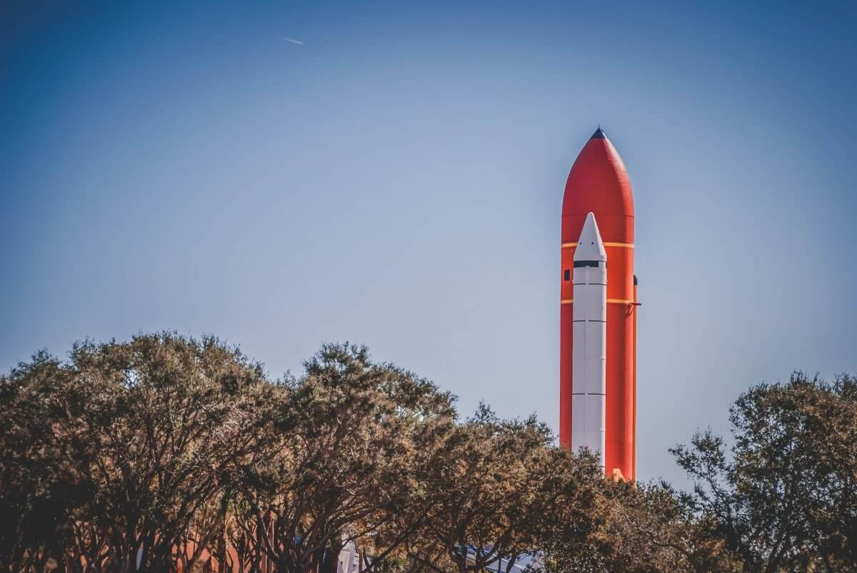 A nose cone of a rocket peeking out over trees. 