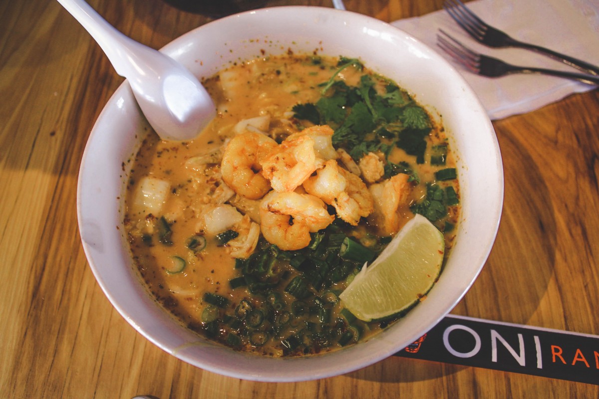 Oni Ramen, one of the best places to eat in Fort Worth, serves Tsunami Ramen shown in this picture. Orange broth topped with grilled shrimp and a lime wedge. 
