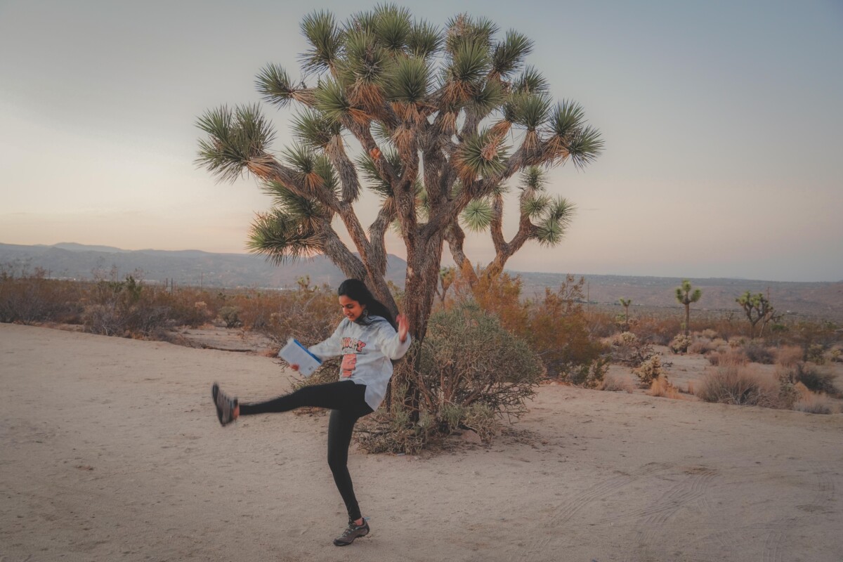 holding a book and dancing in front of a Joshua Tree 